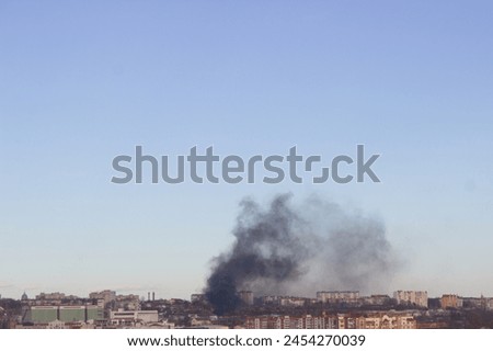 Smoke rising over a cityscape under a blue sky.