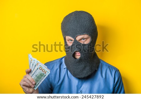 man close up thief in a mask and a blue shirt on a yellow background looks slyly to the camera. Mimicry. Gesture. photo Shoot