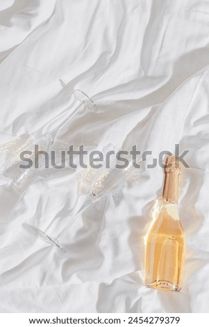 Romance concept, lifestyle photo minimal style, two bright glasses with rainbow shadow, white wine bottle on white bedclothes at home, natural light, top view close up, star filter effect, copyspace