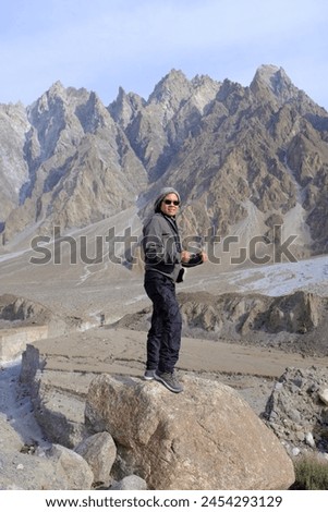 An Asian female tourist posing for a picture with the view of tall mountains in Passu Valley, Gilgit-Baltistan, Pakistan.