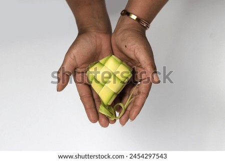 Hand presenting a ketupat pouch, a traditional Indonesian dish made from woven young coconut leaves (janur), isolated on white background