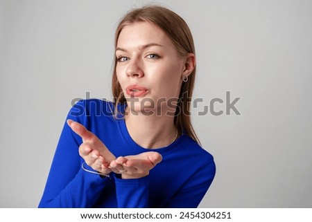 Young Woman in Blue Top Blowing a Kiss Against a Neutral Background.