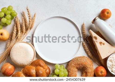 Religious Jewish holiday Shavuot background with dairy products, cheese, bread, wheat crops and empty white plate for text, copy space. Happy Shavuot menu design. Royalty-Free Stock Photo #2454307639