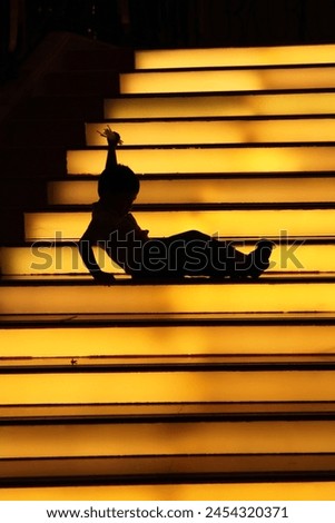 Interior backlight photo view of a silhouette outline isolated shpae of a kid child boy children lying down on bright yellow light glowing stairs starcase slippery fall falling slipped on steps