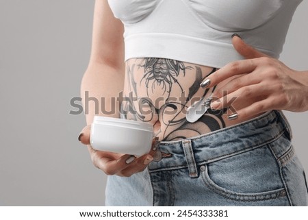 Woman applying healing cream onto her tattoos against grey background, closeup