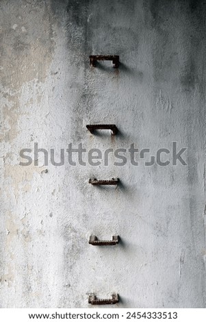 Exterior photo view of an old style ladder made from rusted metal style incrusted inside the wall concrete cement to go up or down to access next level