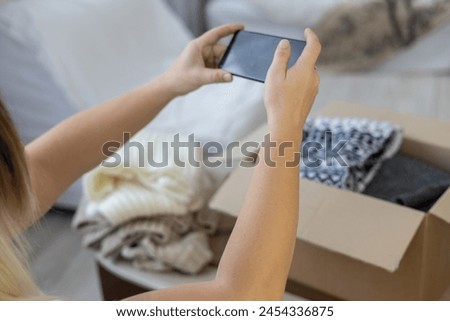 A woman takes pictures of things folded into boxes to sell them on the Internet. Sorting unnecessary things and their second life. A woman sells unnecessary things on the Internet using her phone.
