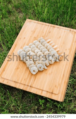 fresh peeled shrimp on skewers lie on a wooden cutting board. summer green grass background