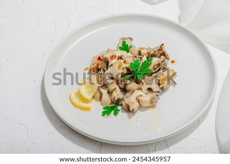 Rapana clam meat with oil, spices and greens. Healthy seafood is rich in omega. Marine decor, hard light, dark shadow, white plaster background, flat lay, close up Royalty-Free Stock Photo #2454345957