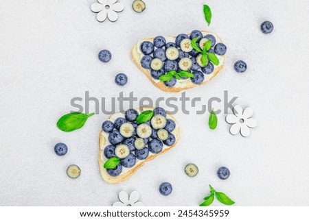 Fresh bread sandwiches with sweet blueberries, cream cheese and basil leaves. Good morning breakfast concept. White stone concrete background, flat lay, top view