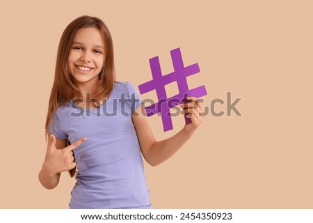 Cute teenage girl pointing at hashtag on beige background