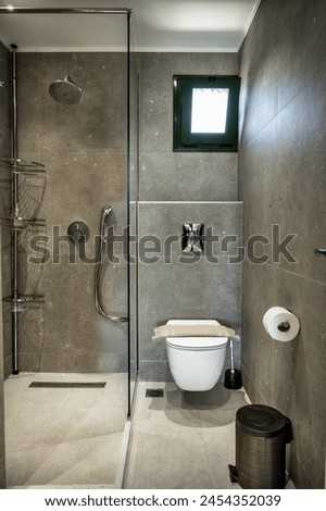 Contemporary bathroom interior design. Walls are adorned with stylish grey tiles. Highlight of the space is the walk-in rain shower, elegantly separated from the toilet area by a sleek glass wall