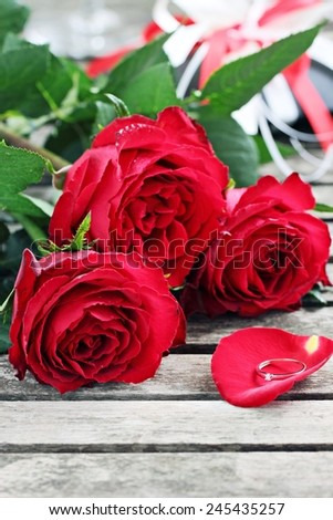 Red roses and a ring on a rustic wooden table. Selective focus.