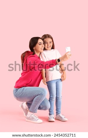 Happy mother with her little daughter taking selfie on pink background