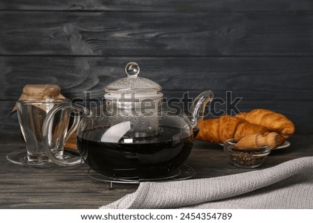 Glass teapot of hot tasty blue tea on black wooden background
