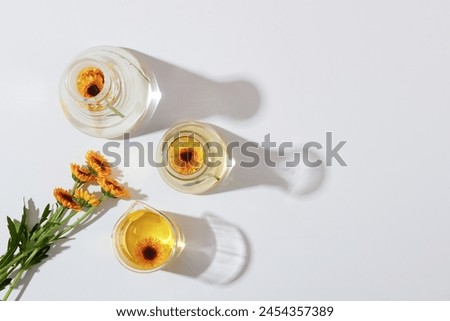 Mockup scene for cosmetic of calendula extract. Top view of fresh calendula flowers on lab glassware with essence decorated on a white background. Minimal concept, copy space