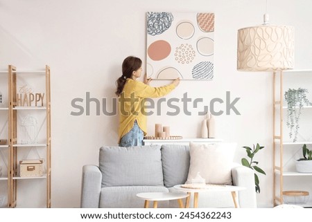 Young pretty woman hanging picture on white wall in living room