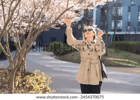 women is taking picture of blossoming cherry on mobile phone on street in spring