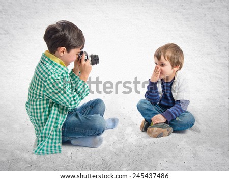 Boy sitting and photographing his friend over textured background 