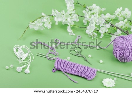 Spring knitting concept. Pattern example, traditional tools, ball of yarn, blooming cherry branch. Creative handmade flat lay, pastel green background, close up Royalty-Free Stock Photo #2454378919