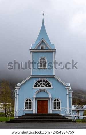 The Blue Church in Seydisfjordur (Seydisfjardarkirkja), exterior view of the bright blue building facade, foggy mountains in the background, Iceland.