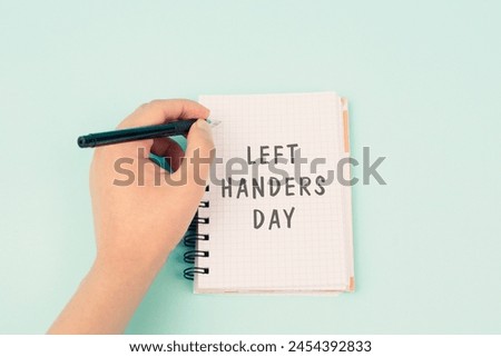 Left handers day is standing on a notebook, writing with the left hand, pen and table  Royalty-Free Stock Photo #2454392833