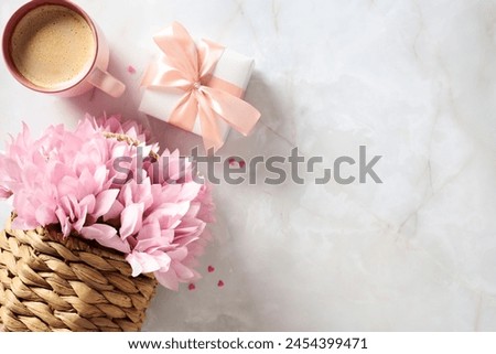 Rattan basket with pink flowers, gift box and cup of coffee, and heart-shaped confetti on stone table. Happy Mother's Day greeting card design. International Women's Day, feminine birthday concept. Royalty-Free Stock Photo #2454399471