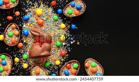Chocolate eggs and rabbit, sugar colored sprinkles on a black background, top view. Easter composition. Easter chocolate bunny. Festive sweet treat. Chocolate figurine. Sweets