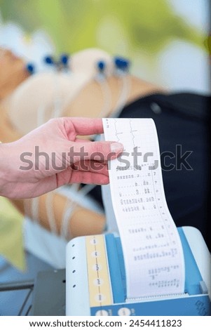 A caregiver is attentively checking a patients vitals with an EKG readout in their hand. Royalty-Free Stock Photo #2454411823