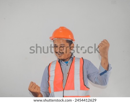 Asian man worker wearing safety helmet lookis happy celebrating his victory by clenching his fists against