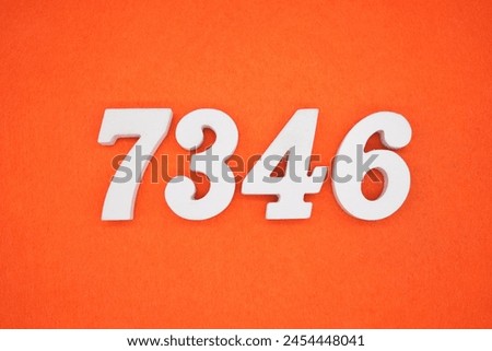 The number 7346 is made from white painted wood placed on a background of orange paper.