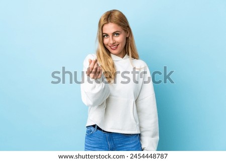 Young Uruguayan blonde woman over isolated blue background making money gesture