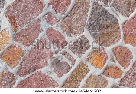 It's the close up view of the colorful wall. Its photo of multicolor stonewall. It is photo of multicolored srone wall. its view of red sidewalk. It's view of the mosaic stonewall