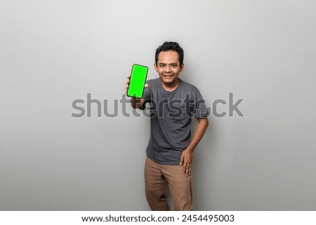 Asian man in gray is showing a green screen smartphone as if recommending something