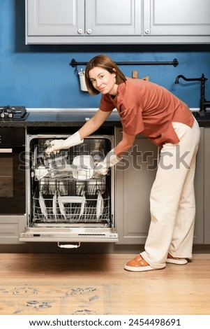 Busy housewife putting dirty plates in dishwasher machine in the kitchen. Household and exhausting cleaning day concept Royalty-Free Stock Photo #2454498691