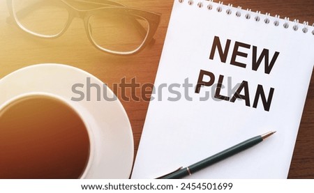 NEW PLAN - text on paper with cup of coffee and glasses on wooden background in sinlight.
