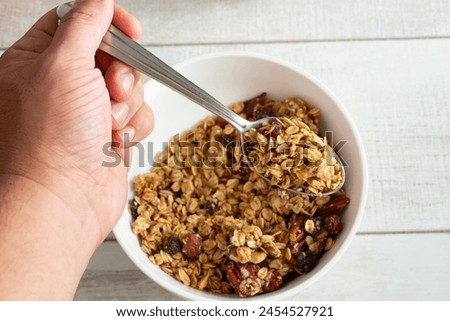 A top down view of a hand holding a spoonful of granola cereal.