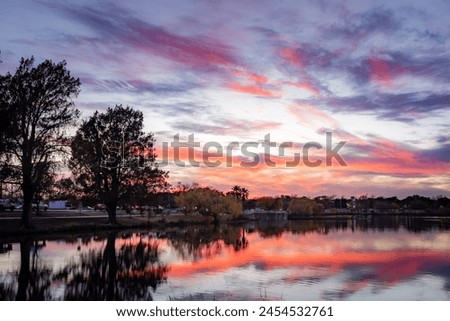 Dramatic pink and orange sunset clouds reflected on a calm and peaceful lake. Photo taken along the treelined horizon  at Woodlawn Lake San Antonio Texas