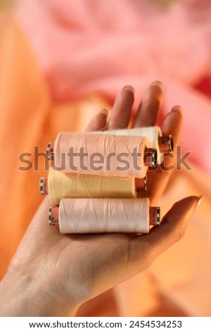 Hand holding Raw White Polyester FDY Yarn spool, Polyester Filament Yarn spool.PET fiber Yarn,spun polyester sewing thread with peach background.               Royalty-Free Stock Photo #2454534253