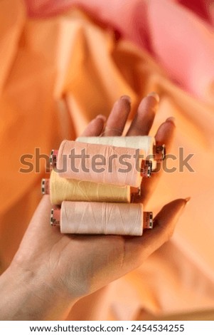 Hand holding Raw White Polyester FDY Yarn spool, Polyester Filament Yarn spool.PET fiber Yarn,spun polyester sewing thread with peach background.               Royalty-Free Stock Photo #2454534255