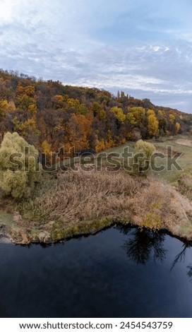 Aerial calm river shore in colorful autumn valley with cloudy sky in Ukraine