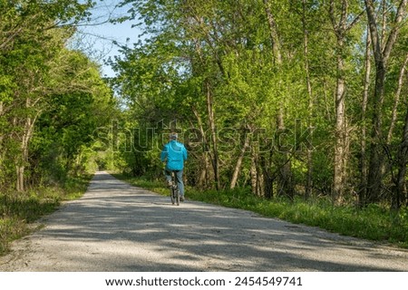 Male cyclist is riding a folding bike on Katy Trail near Rocheport, Missouri, spring scenery. The Katy Trail is 237 mile bike trail converted from an old railroad. Royalty-Free Stock Photo #2454549741