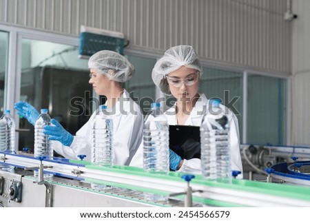 Two female worker working inspecting quality clean purified drinking plastic bottled water inside automated conveyor belt production line in drinking water factory