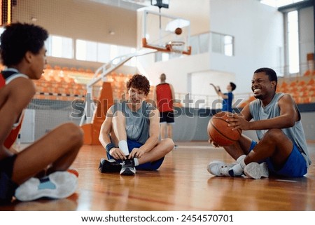 Happy basketball players communicating while relaxing on the court during sports training. Focus is on player tying his shoelace. 
