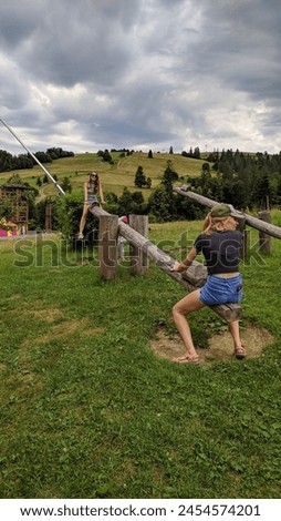 Two girls ride on a large wooden swing against the backdrop of green mountain slopes and forests. Photo.
 Royalty-Free Stock Photo #2454574201