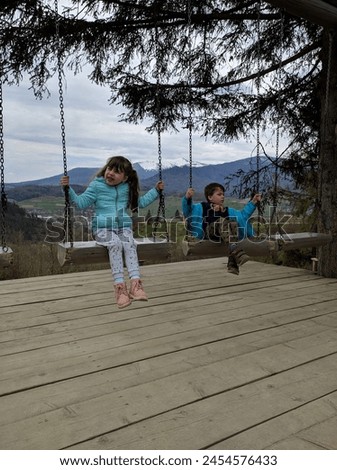 A boy and a girl ride on a swing against the background of a mountain range and a mountain village, family recreation in the fresh air. Photo.