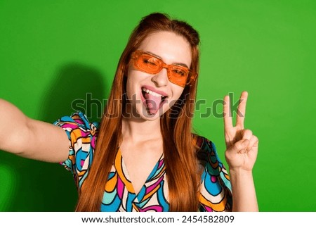 Portrait of pretty young girl take selfie show v-sign tongue out wear top isolated on bright green color background