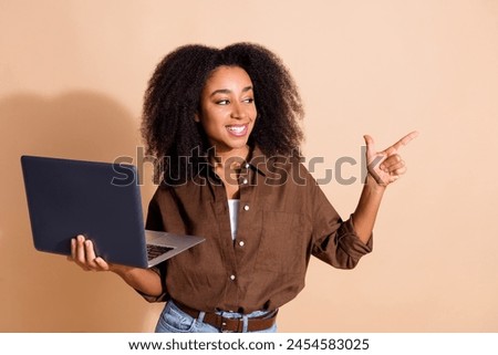 Photo of smart optimistic girl wear brown blouse look directing at sale empty space holding laptop isolated on pastel color background