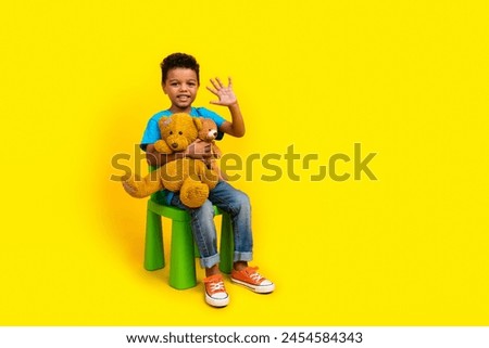 Full body photo of multiethnic multinational child dressed blue t-shirt hold teddy bears waving palm isolated on vibrant yellow background Royalty-Free Stock Photo #2454584343