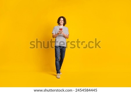 Full size portrait of nice young man chatting smart phone wear striped t-shirt isolated on yellow color background